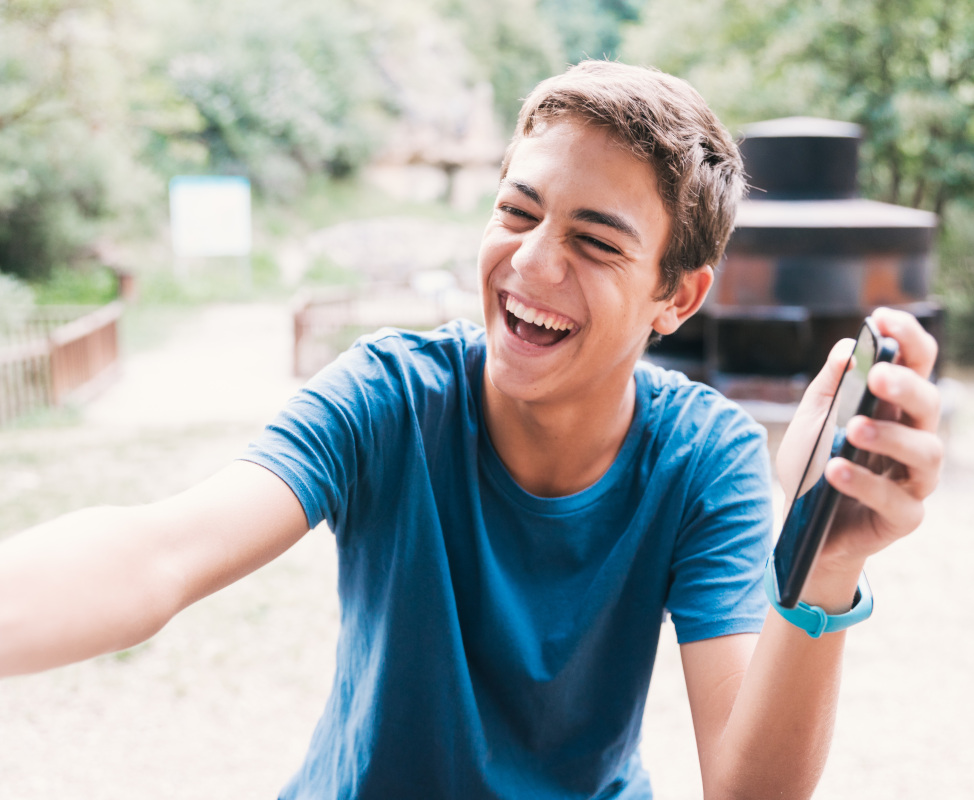 Teenage,Boy,Sitting,Outdoors,Laughing,Sharing,Smartphone,Screen,With,Someone